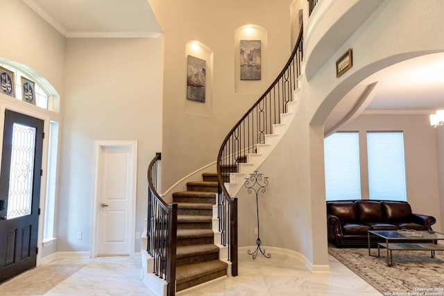 entrance foyer with baseboards, ornamental molding, stairway, arched walkways, and a high ceiling