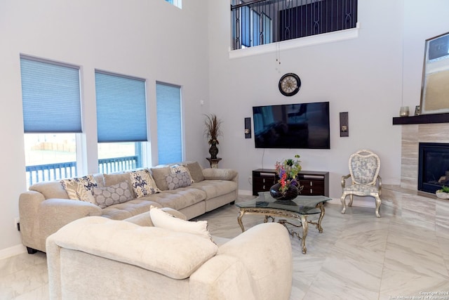 living room with marble finish floor, baseboards, a tiled fireplace, and a towering ceiling