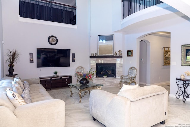 living room with baseboards, marble finish floor, a towering ceiling, arched walkways, and a tiled fireplace