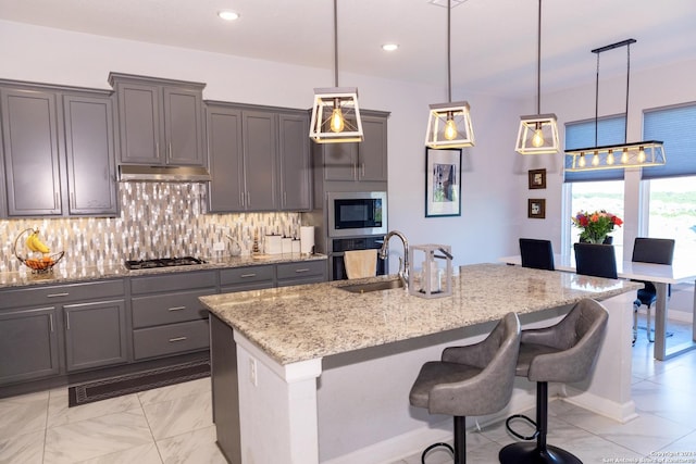 kitchen with a breakfast bar, backsplash, a sink, light stone counters, and appliances with stainless steel finishes