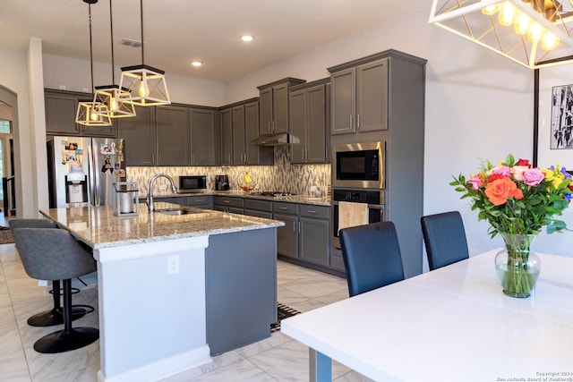 kitchen featuring decorative backsplash, stainless steel appliances, a sink, light stone counters, and a kitchen breakfast bar