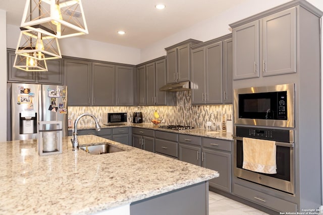 kitchen featuring stainless steel appliances, under cabinet range hood, backsplash, a sink, and a notable chandelier