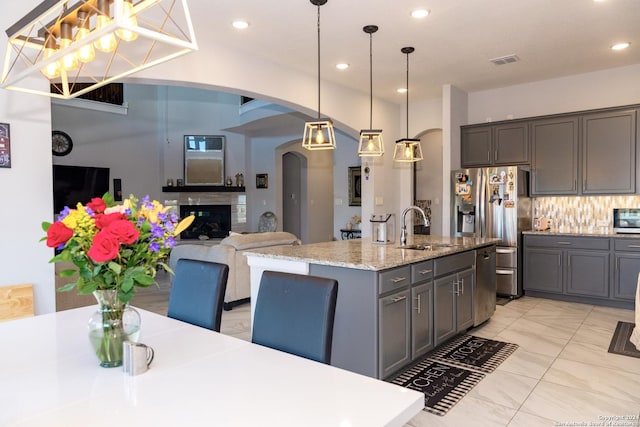 kitchen with stainless steel fridge, gray cabinetry, backsplash, a sink, and arched walkways