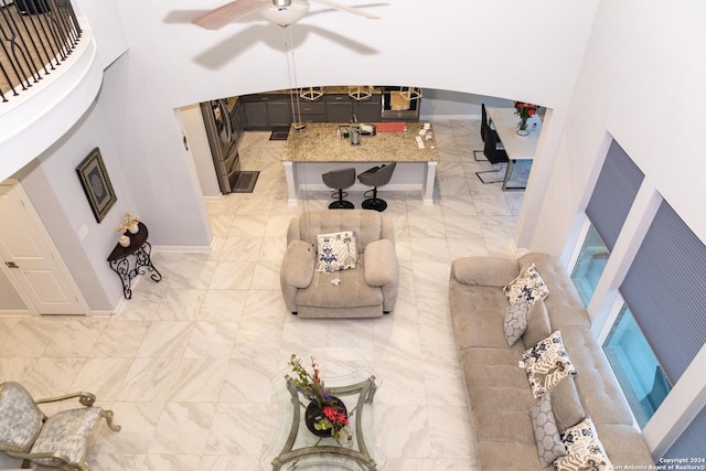 living room featuring marble finish floor, a ceiling fan, baseboards, and a high ceiling