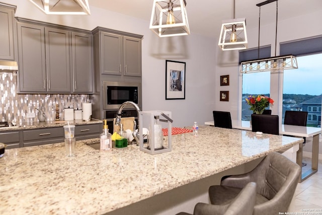 kitchen featuring light stone countertops, a kitchen bar, gray cabinetry, under cabinet range hood, and built in microwave