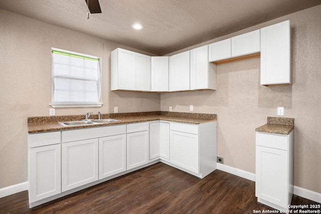 kitchen featuring baseboards, a textured ceiling, dark wood finished floors, a sink, and white cabinets