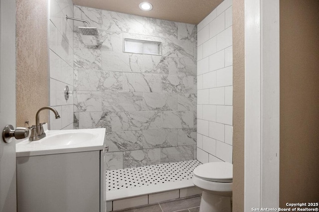 bathroom with a tile shower, toilet, and vanity
