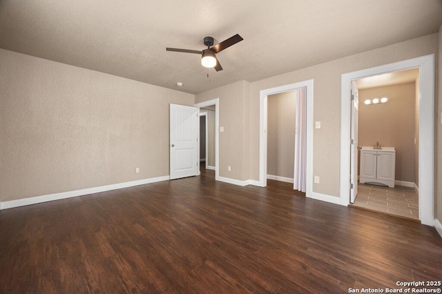 unfurnished bedroom with dark wood finished floors, baseboards, ceiling fan, and ensuite bath