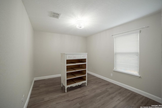 unfurnished room with visible vents, a textured ceiling, baseboards, and wood finished floors