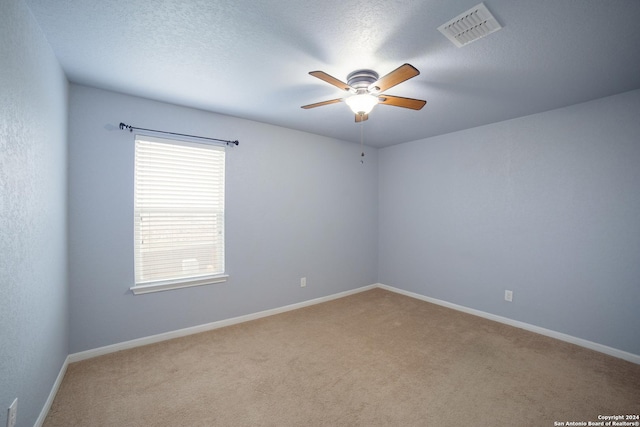 carpeted spare room with a textured ceiling, visible vents, baseboards, and a ceiling fan