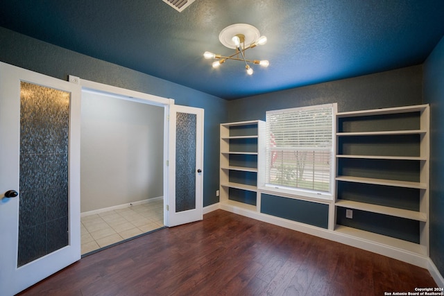 unfurnished bedroom featuring a textured ceiling, wood finished floors, baseboards, and a chandelier