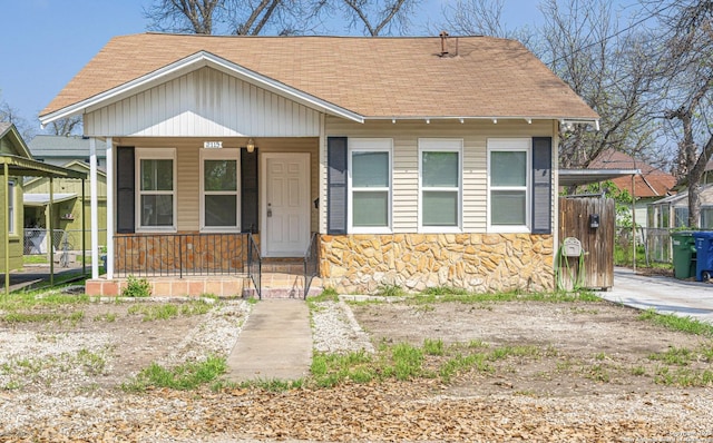 bungalow with stone siding, a shingled roof, fence, and a porch