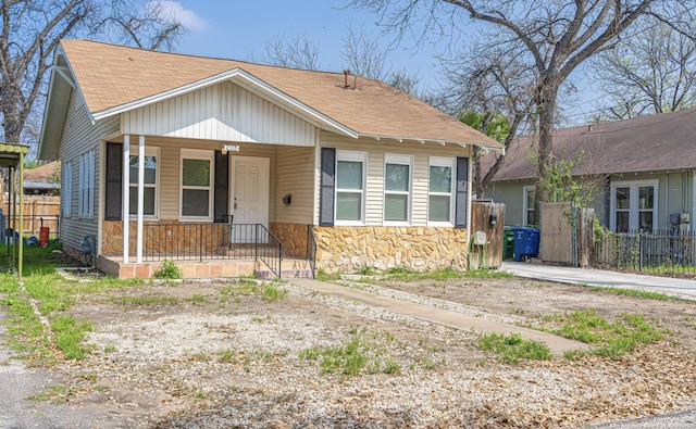 bungalow with a shingled roof, fence, stone siding, and a porch