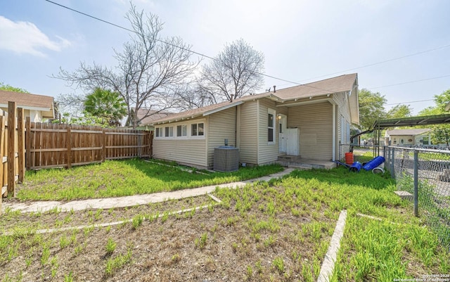 rear view of house with a fenced backyard, central AC, and a yard