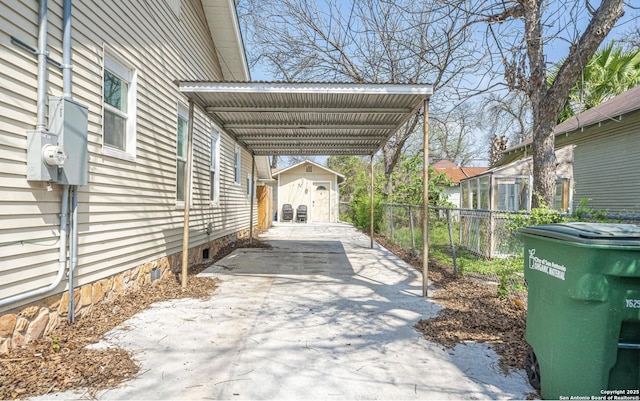 view of vehicle parking with an attached carport, driveway, a storage unit, and fence