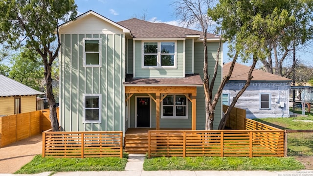 traditional home with board and batten siding, a shingled roof, covered porch, and a fenced front yard