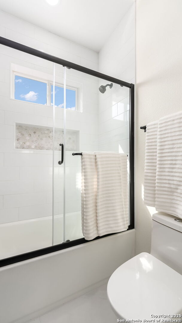 bathroom with combined bath / shower with glass door and toilet