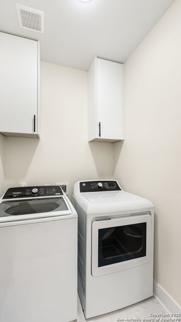 washroom featuring baseboards, cabinet space, visible vents, and washer and clothes dryer