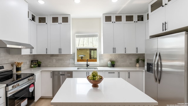 kitchen with light countertops, stainless steel appliances, backsplash, a sink, and wall chimney exhaust hood