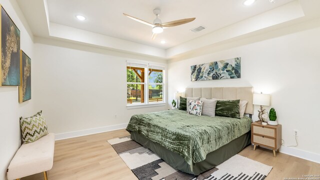 bedroom with visible vents, light wood-type flooring, and a raised ceiling