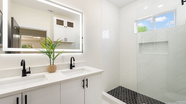 full bathroom featuring visible vents, a sink, a tile shower, and double vanity