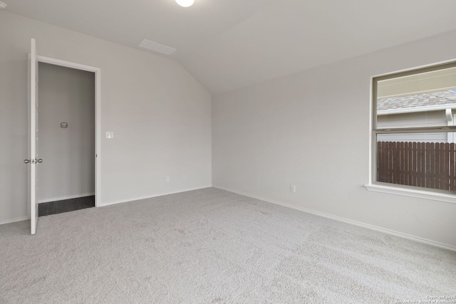 carpeted spare room featuring baseboards and vaulted ceiling