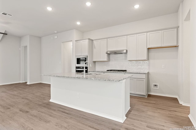 kitchen featuring gas cooktop, under cabinet range hood, built in microwave, visible vents, and a sink