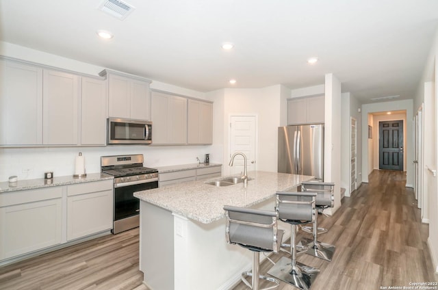 kitchen featuring an island with sink, a sink, a kitchen breakfast bar, appliances with stainless steel finishes, and light wood-style flooring