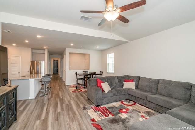 living room with lofted ceiling, ceiling fan, visible vents, and light wood finished floors