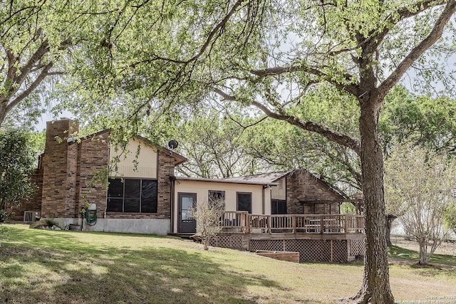 rear view of property with brick siding, a deck, a yard, and a chimney