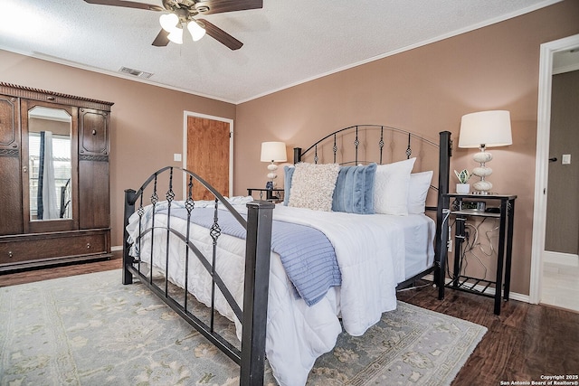bedroom featuring a textured ceiling, visible vents, crown molding, baseboards, and wood finished floors