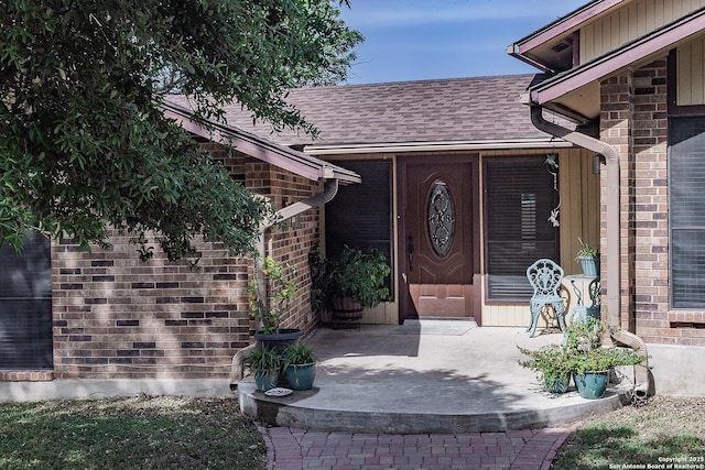 entrance to property featuring brick siding and roof with shingles