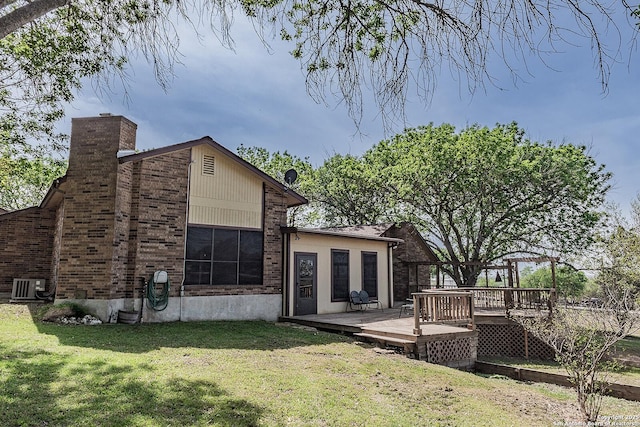 back of property with central AC unit, a wooden deck, a chimney, brick siding, and a yard