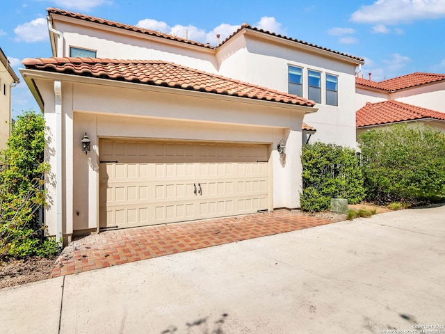 mediterranean / spanish-style home with a tile roof, stucco siding, a garage, and driveway