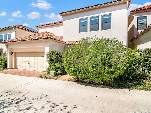 mediterranean / spanish house featuring a tile roof, stucco siding, an attached garage, and driveway