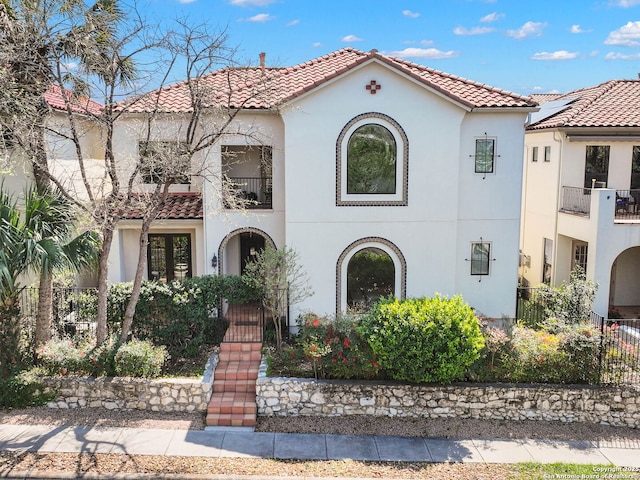 mediterranean / spanish home featuring stucco siding, fence, a tiled roof, and a balcony