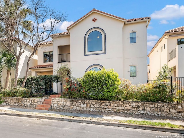 mediterranean / spanish-style home with stucco siding, fence, and a tiled roof