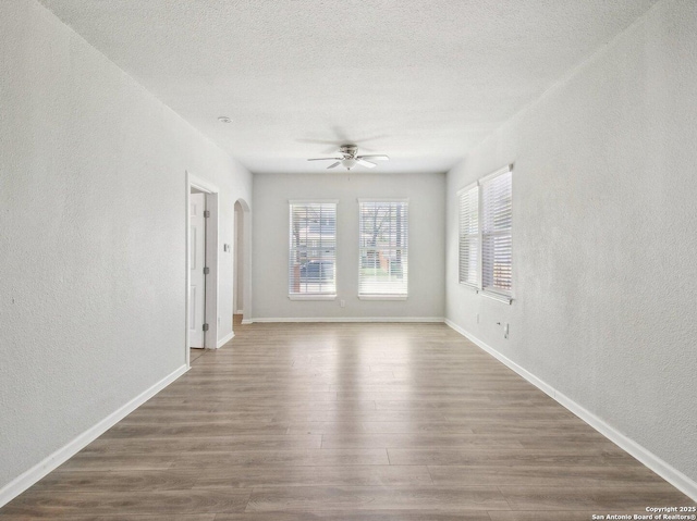 unfurnished room featuring baseboards, a textured ceiling, arched walkways, ceiling fan, and wood finished floors