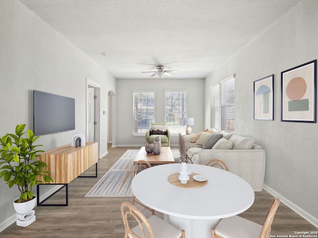 dining space featuring a textured wall, baseboards, arched walkways, a ceiling fan, and wood finished floors