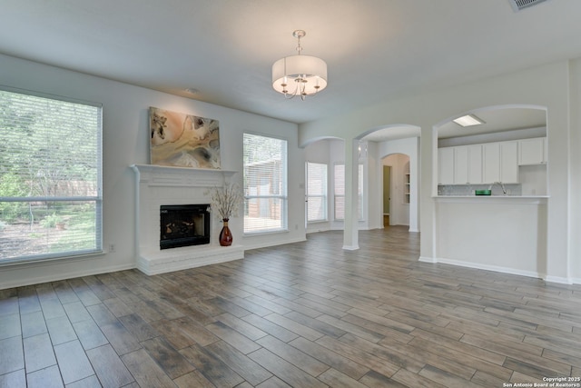 7609 Highland Park, San Antonio, TX 78250 - unfurnished living room featuring a brick fireplace, wood finished floors, a chandelier, arched walkways, and baseboards