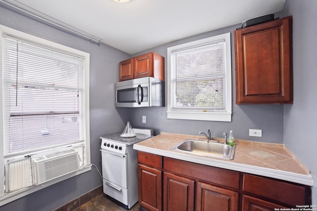 kitchen featuring stone finish floor, tile counters, stainless steel microwave, a sink, and white range with electric stovetop