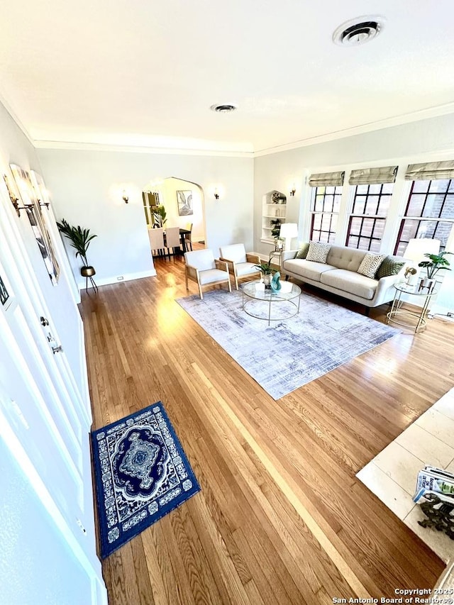 living area featuring crown molding, visible vents, wood finished floors, and arched walkways