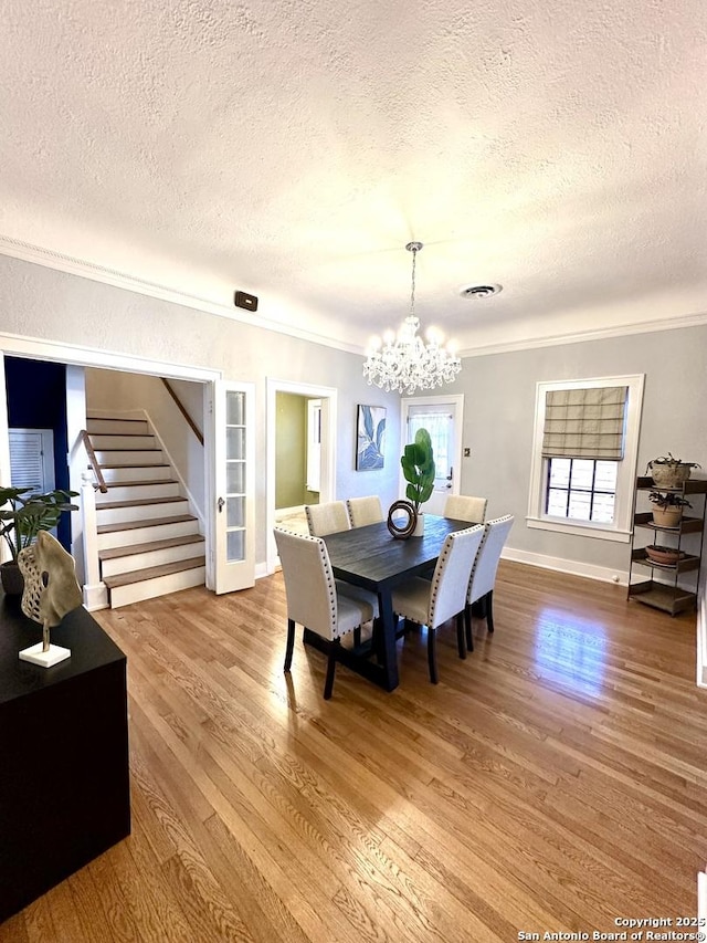 dining room with crown molding, stairs, a chandelier, visible vents, and wood finished floors