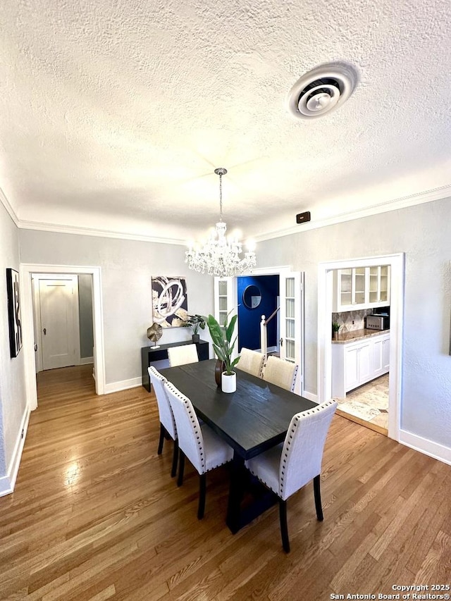 dining area featuring a notable chandelier, light wood-style flooring, baseboards, visible vents, and ornamental molding