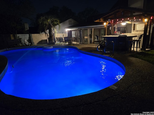 pool at twilight featuring outdoor dry bar, a patio area, and an outdoor pool
