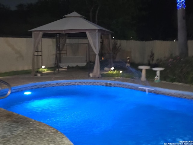 pool at night with a gazebo, a fenced in pool, and a fenced backyard