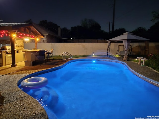 pool at night featuring a gazebo, outdoor dry bar, fence, a patio, and a fenced in pool