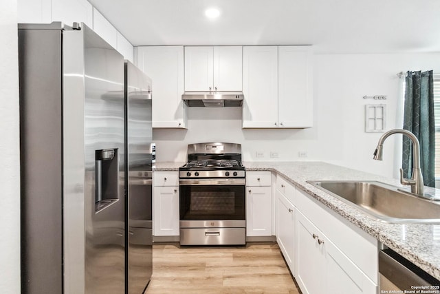kitchen with a sink, appliances with stainless steel finishes, under cabinet range hood, white cabinets, and light wood-style floors