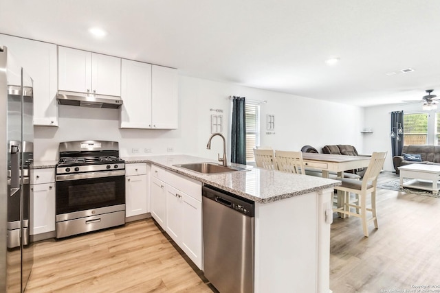 kitchen featuring a peninsula, stainless steel appliances, under cabinet range hood, a sink, and open floor plan