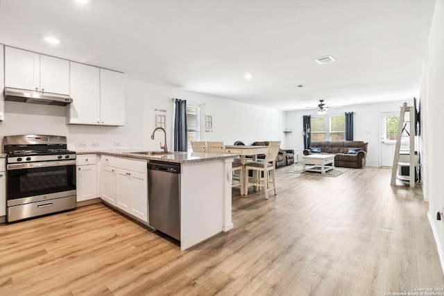 kitchen with a sink, appliances with stainless steel finishes, a peninsula, open floor plan, and under cabinet range hood
